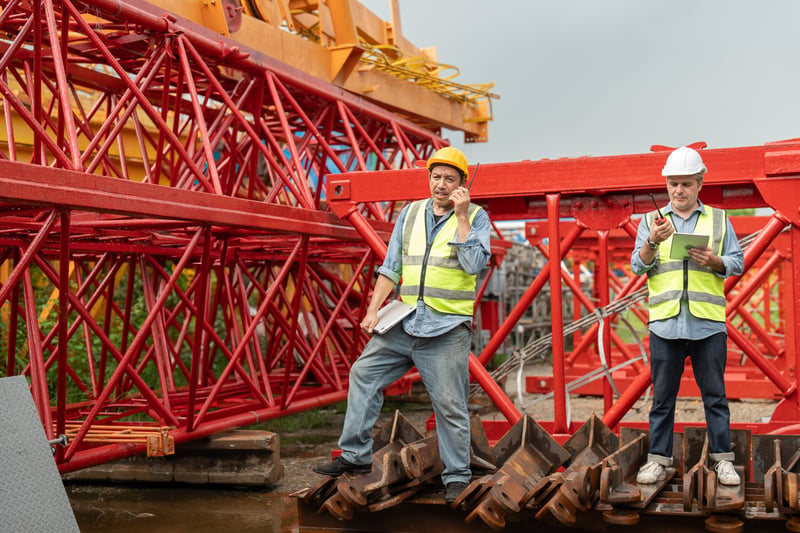 Site manager uses walkie-talkie and laptop near red tower craneklingsup