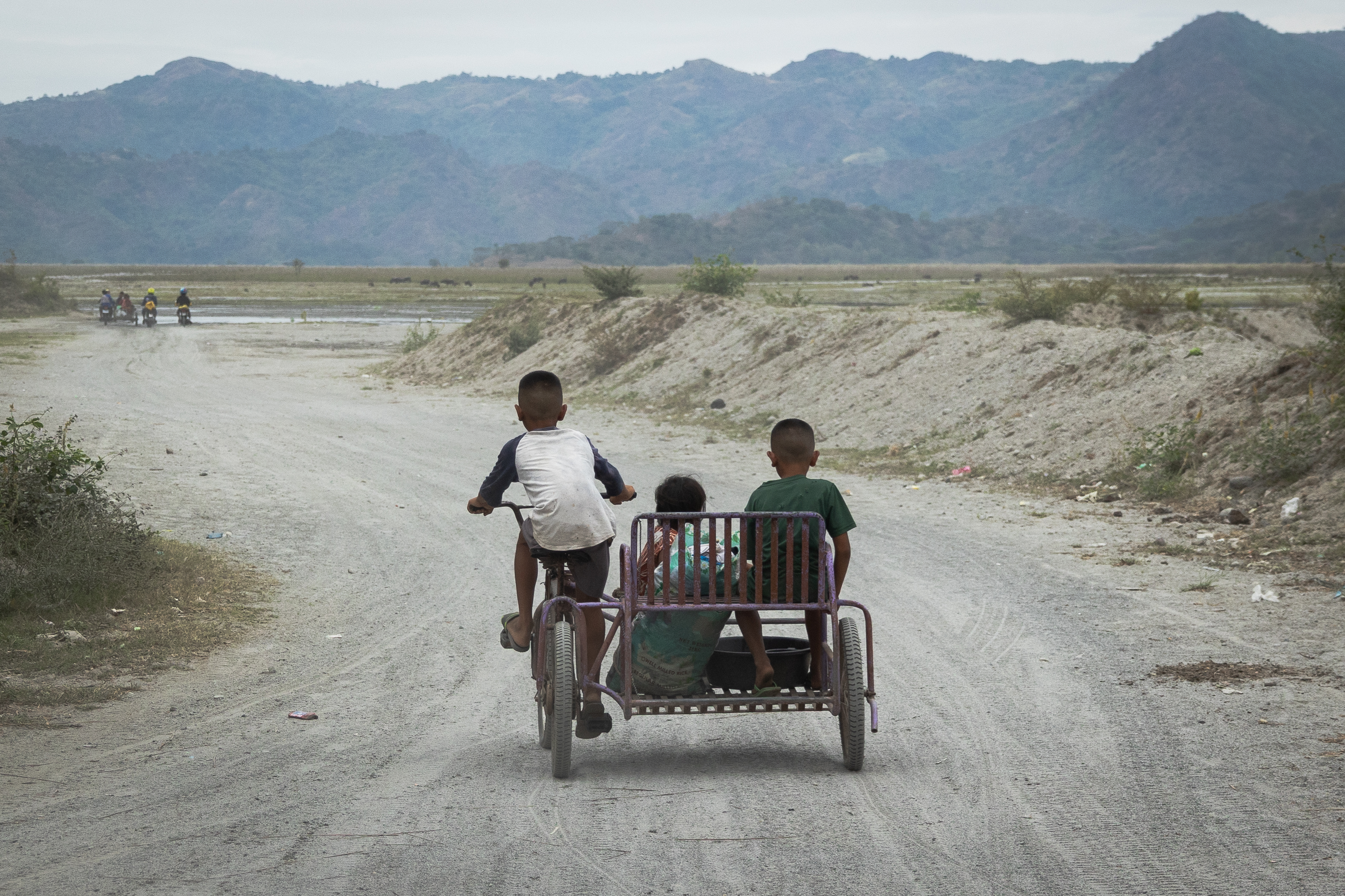 Three Filipino kids riding down a rural dirt road
