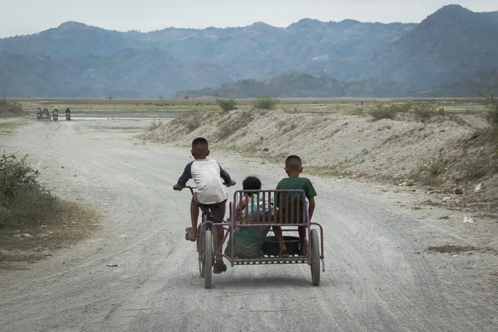 Three Filipino kids riding down a rural dirt road