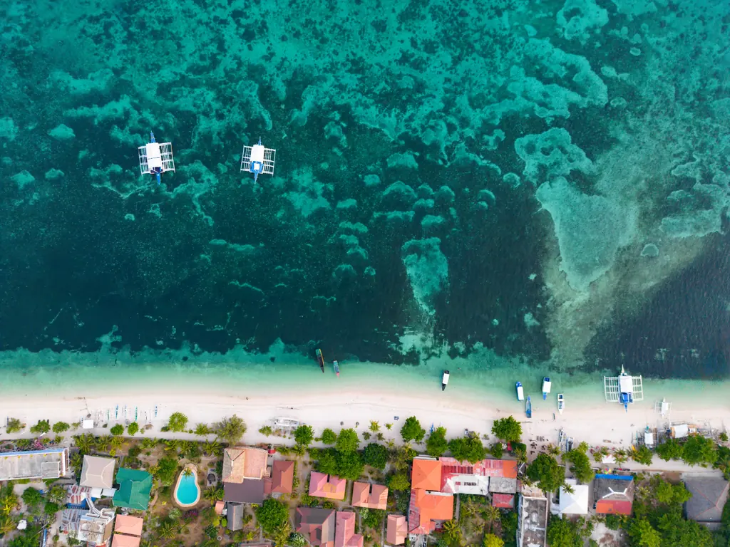 a beach area with several boats in the water and people on shore: Mapascua Island, Philippines
