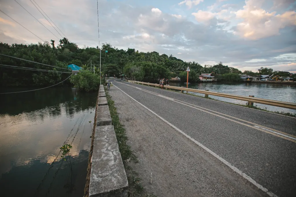 A serene road bridge crossing over a tranquil river surrounded by lush greenery and a scenic sky.
