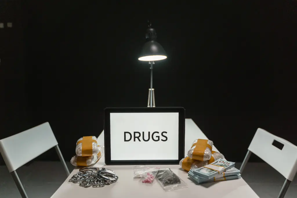 A dimly lit room with a sign displaying 'DRUGS' surrounded by money and illegal substances.