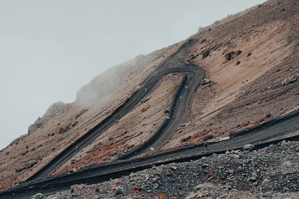 A winding road traverses a barren, rocky mountain with fog above.