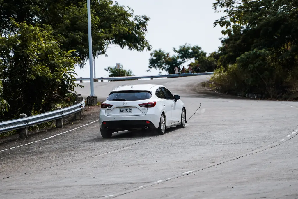 A white car navigates a curving mountain road amidst lush greenery in Mangatarem, Ilocos Region, Philippines.