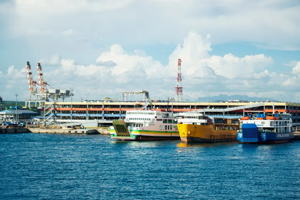 Vibrant ferries docked at a bustling urban port under a bright sky with scattered clouds.