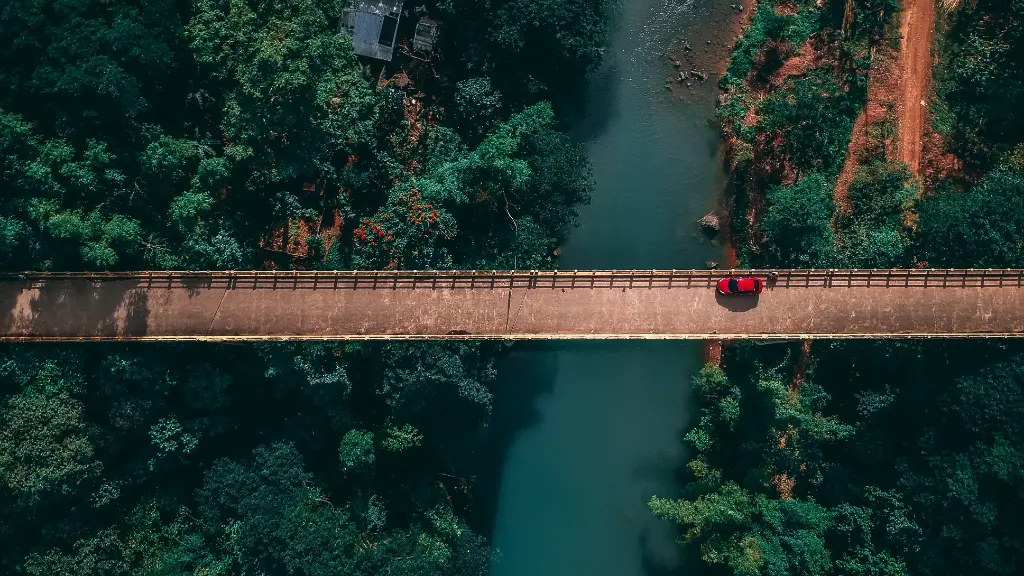 A breathtaking aerial view of a car crossing a bridge over a river surrounded by lush green forest in Norzagaray, Philippines.