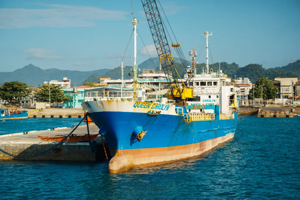 A vibrant blue cargo ship docked at a port terminal with mountains in the background.