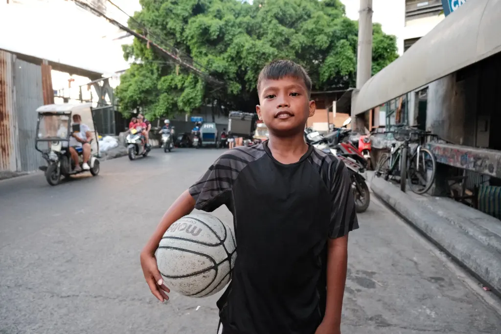 A young boy holding a basketball in an urban Philippine street setting, portraying street culture.