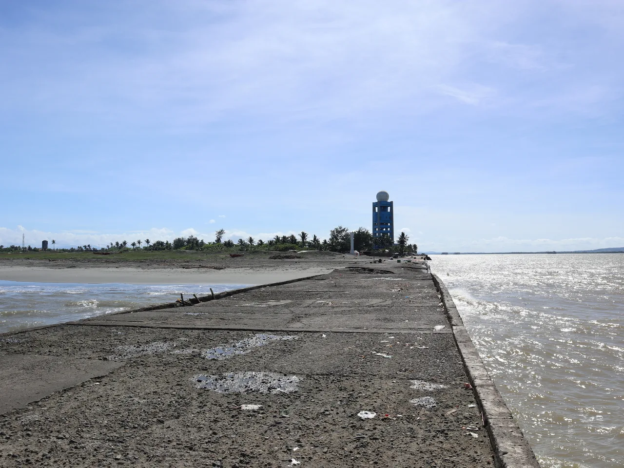 Blick über eine verwitterte Betonmole auf Aparris Küste, Wasser und einen Turm im Hintergrund