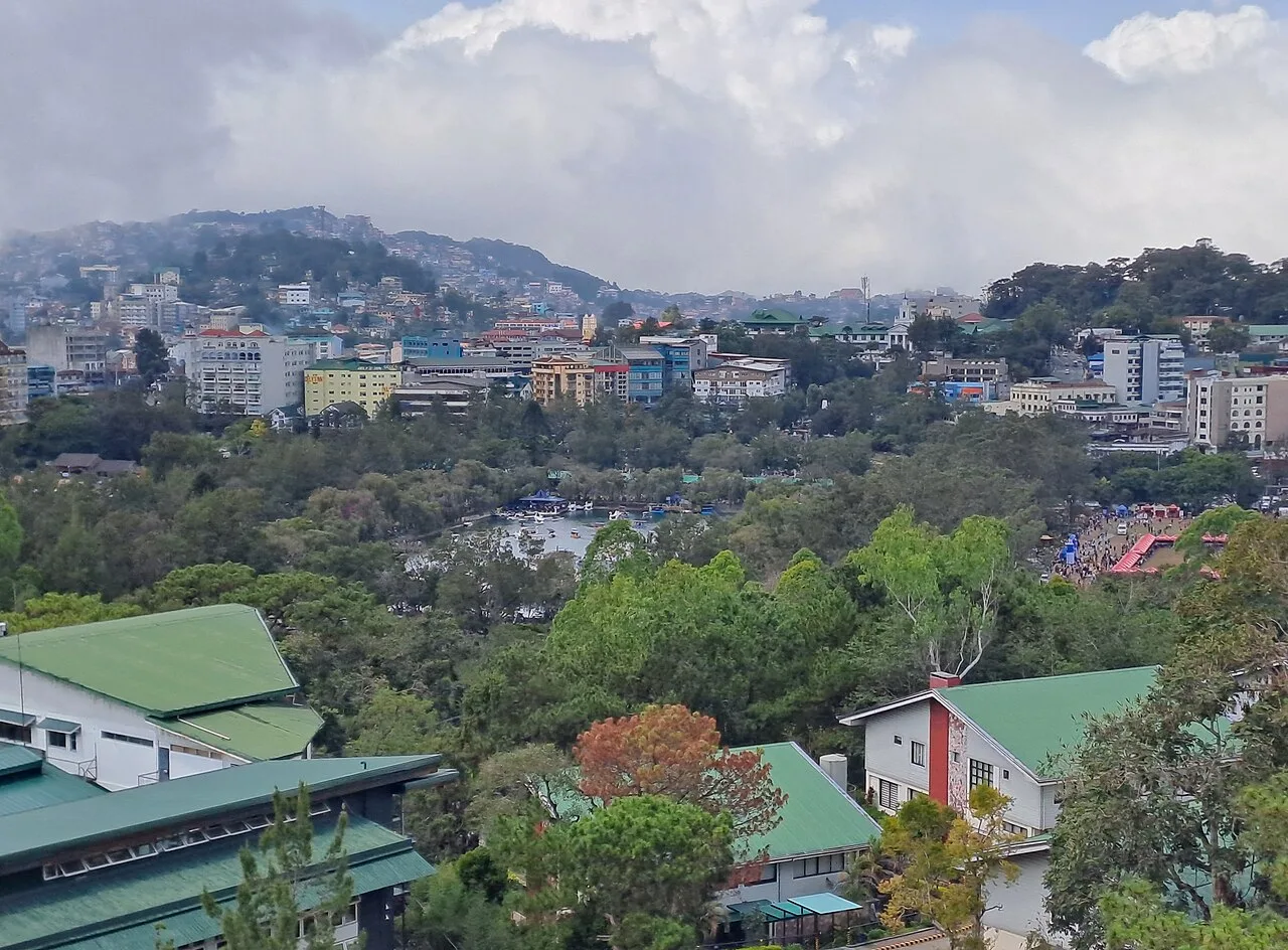 Blick über den baumreichen Burnham Park auf dicht bebaute Hügel von Baguio