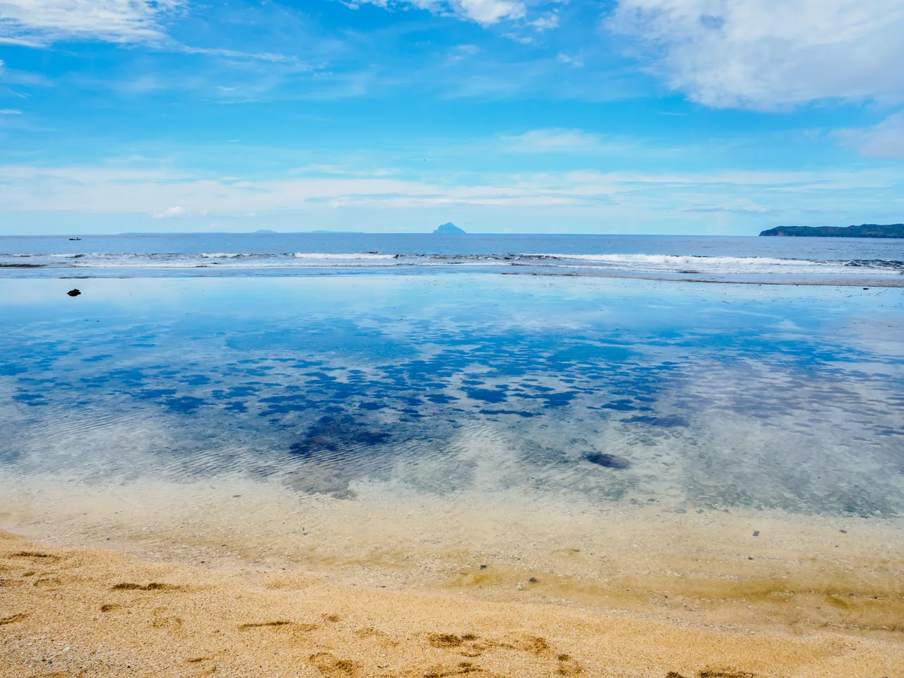 Heller Sand und Wasser am Maydangeb Beach mit entfernten Inselkonturen am Horizont