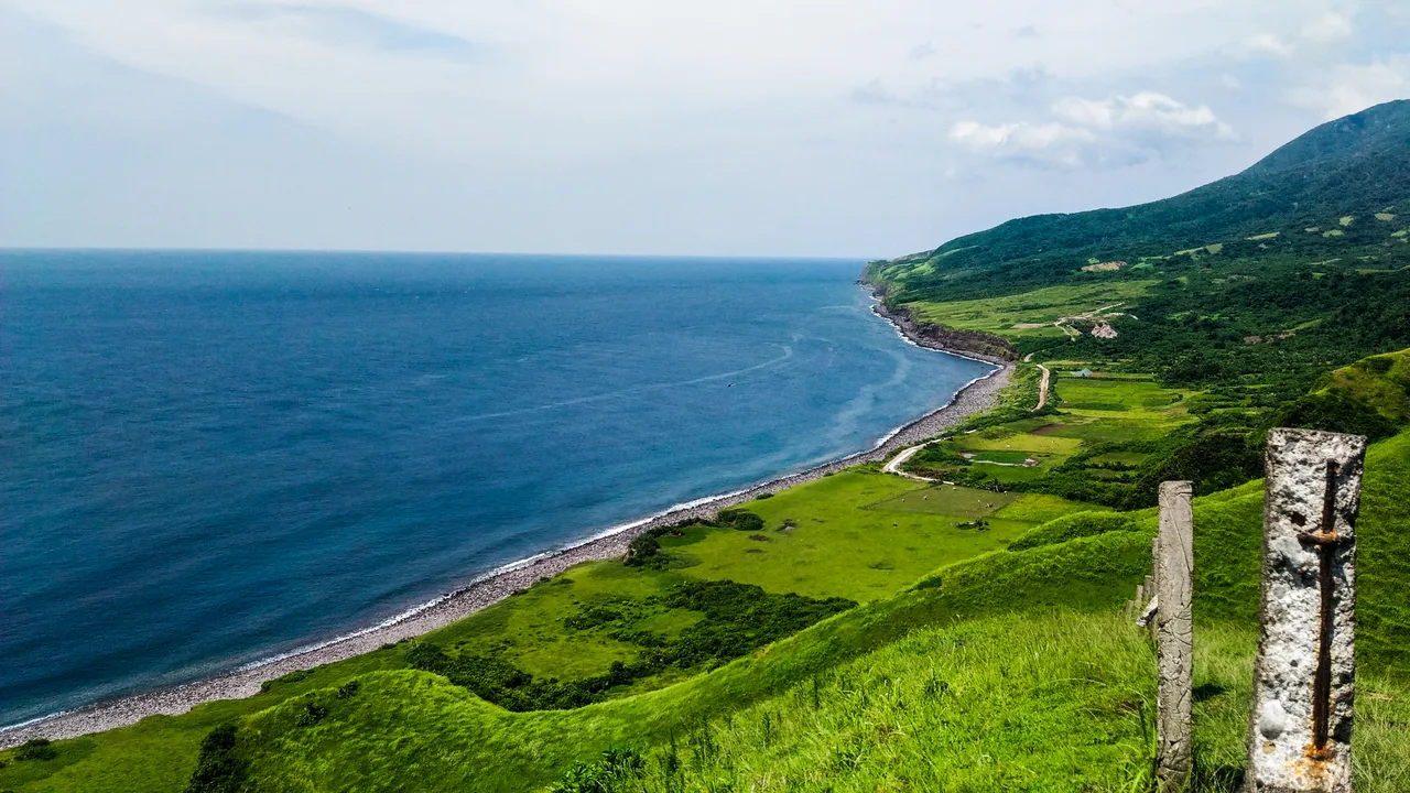 Blick von grünen Hügeln über eine lange steinige Küste und das Meer