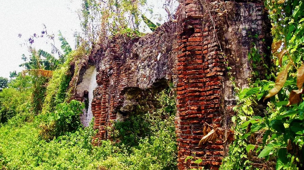 Bewachsene Backsteinmauern und offene Bögen der alten Kirchenruine in Camalaniugan