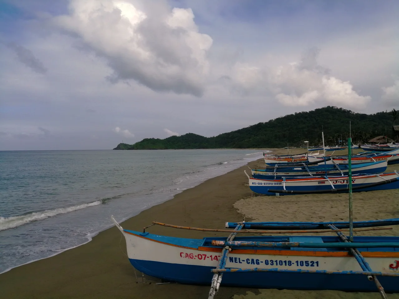 Auslegerboote auf dem Sandstrand von Claveria vor einer bewaldeten Küste