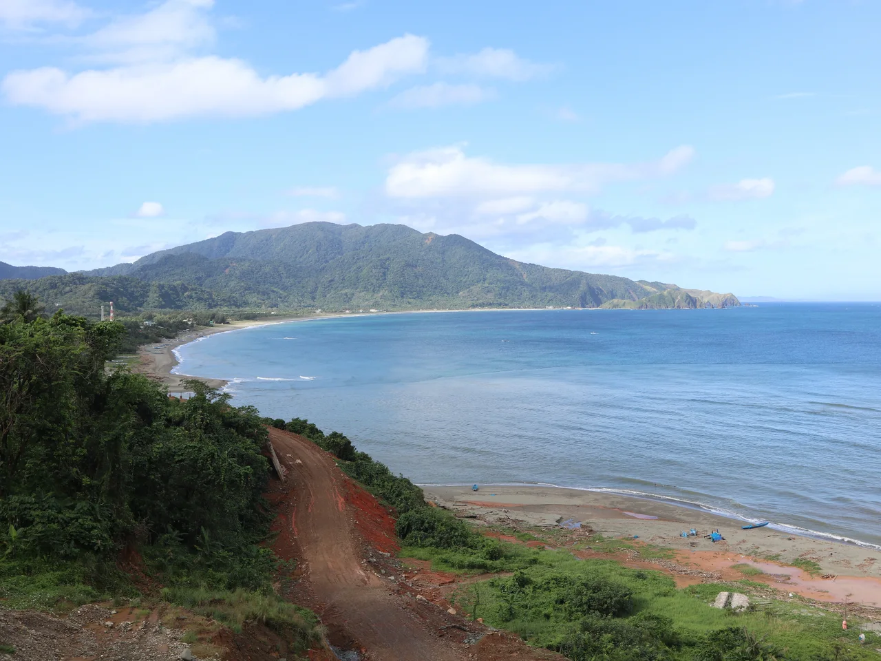 Blick über eine weite Bucht bei Claveria mit Sandstrand, Hügeln und unbefestigtem Weg im Vordergrund