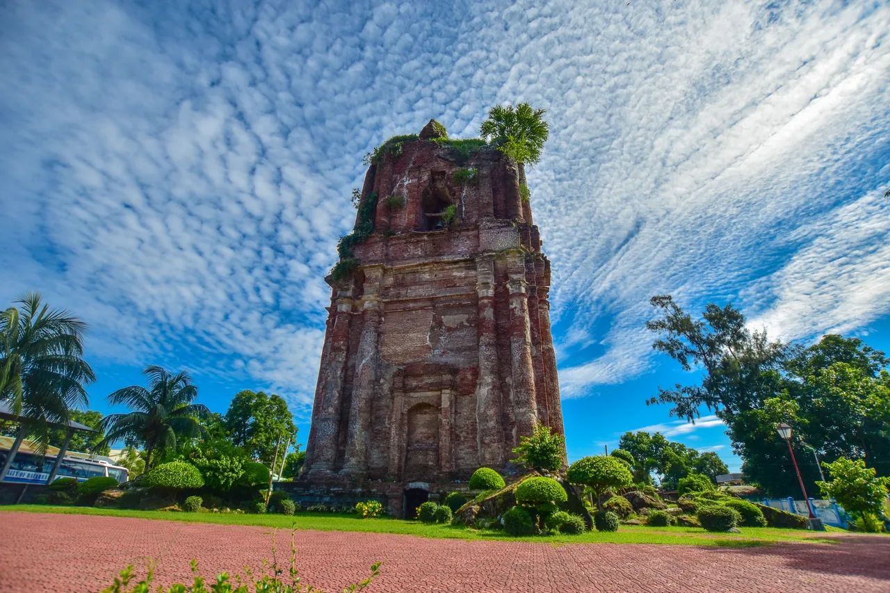Historischer Glockenturm ohne Kuppel in Bacarra mit Vegetation unter gemustertem Wolkenhimmel