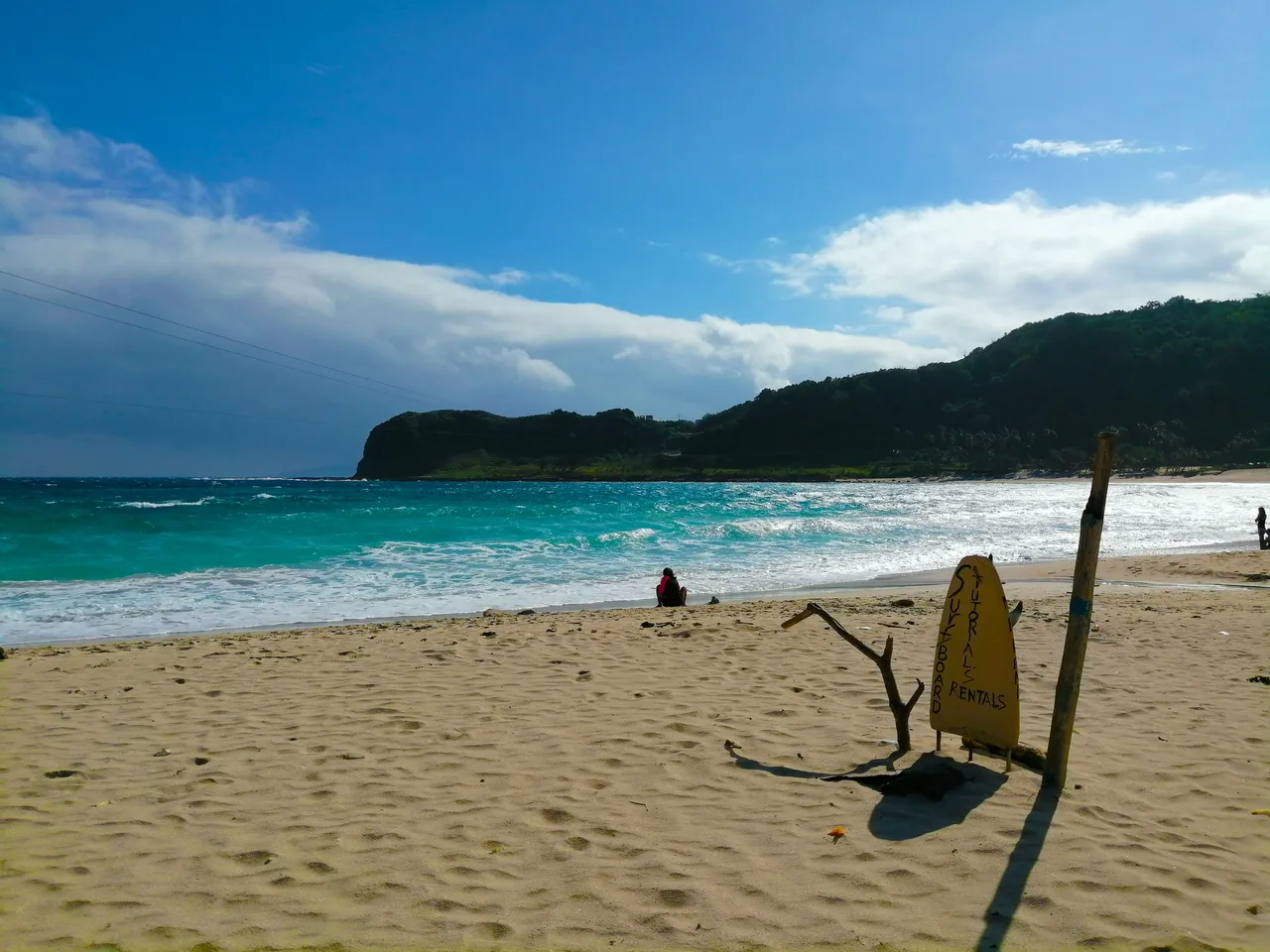 Blue Lagoon in Pagudpud mit Brandung, bewaldeter Küste und einem Verleihschild im Vordergrund