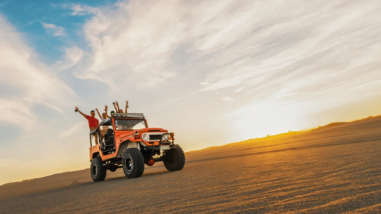 Orangefarbener Geländewagen mit Besuchern auf den Sanddünen von Paoay im Abendlicht