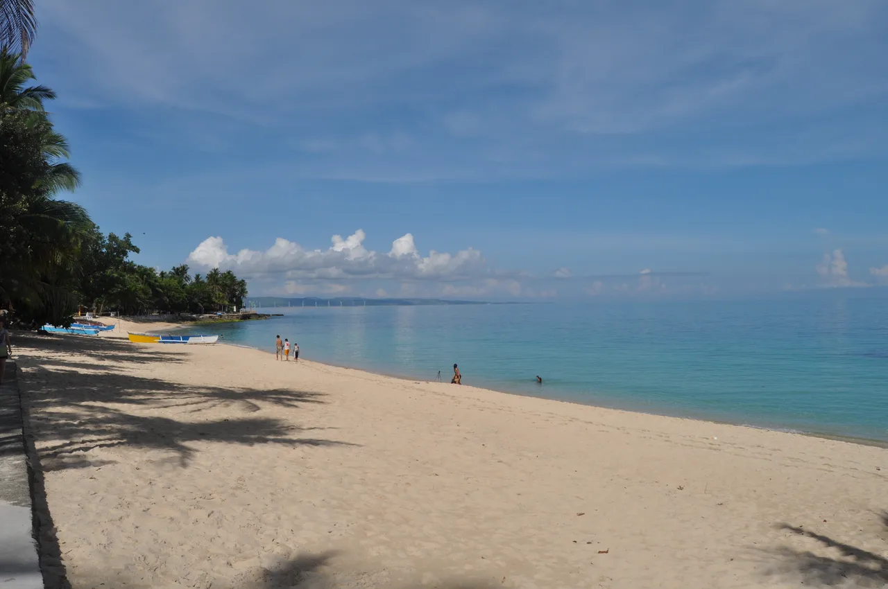 Saud Beach mit hellem Sand, Palmen, Booten und einigen Besuchern