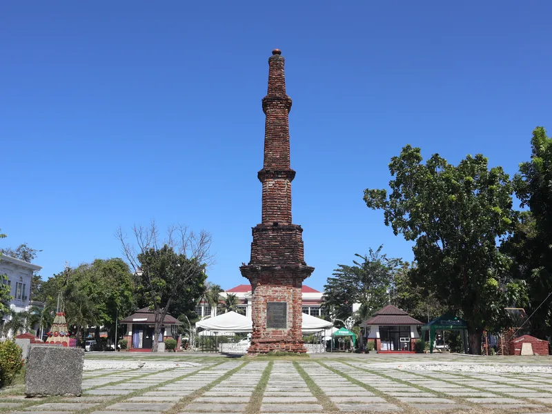 Hoher Backsteinobelisk des Tobacco Monopoly Monument vor Bäumen und Gebäuden im Aurora Park