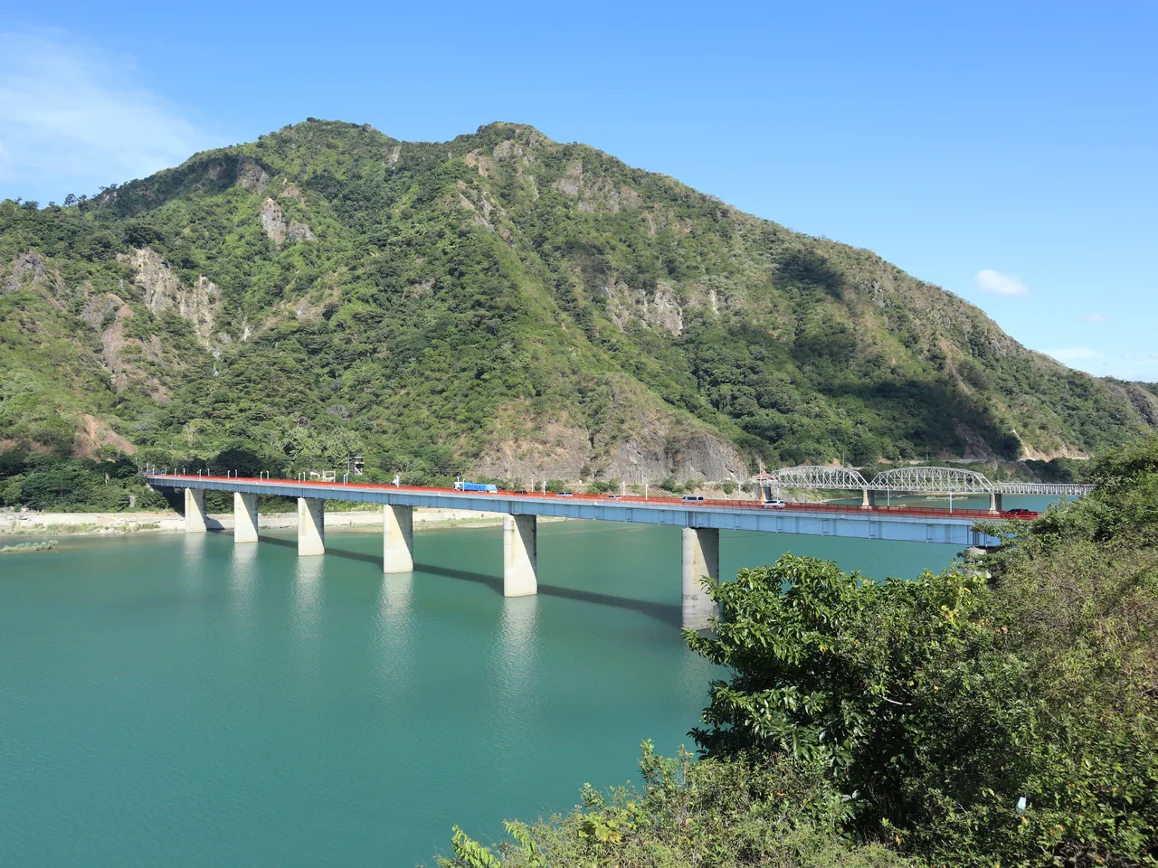 Straßenbrücke über den Abra River mit einer Fachwerkbrücke dahinter und bewaldeten Bergen