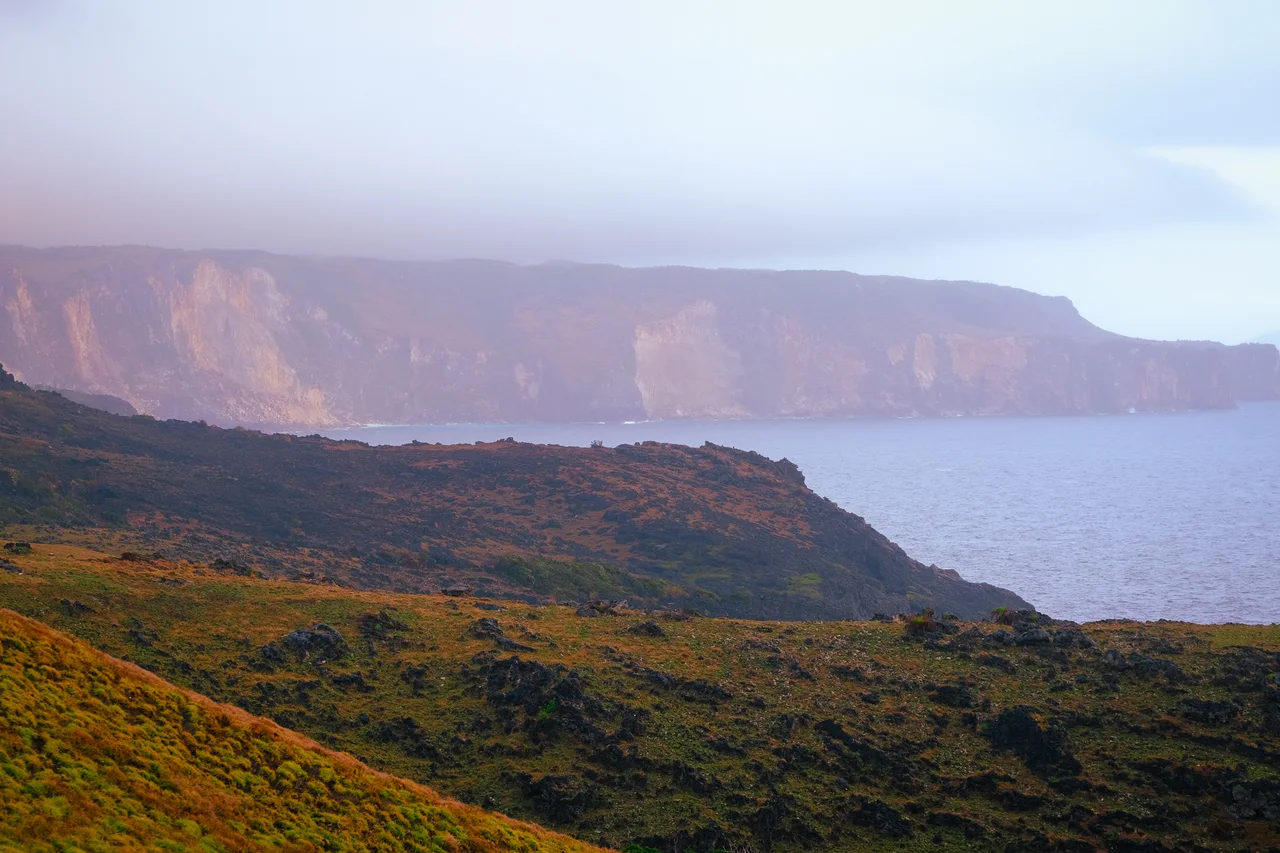 Grasbewachsene Felsen vor dem Meer und den hohen Rapang-Klippen auf Itbayat
