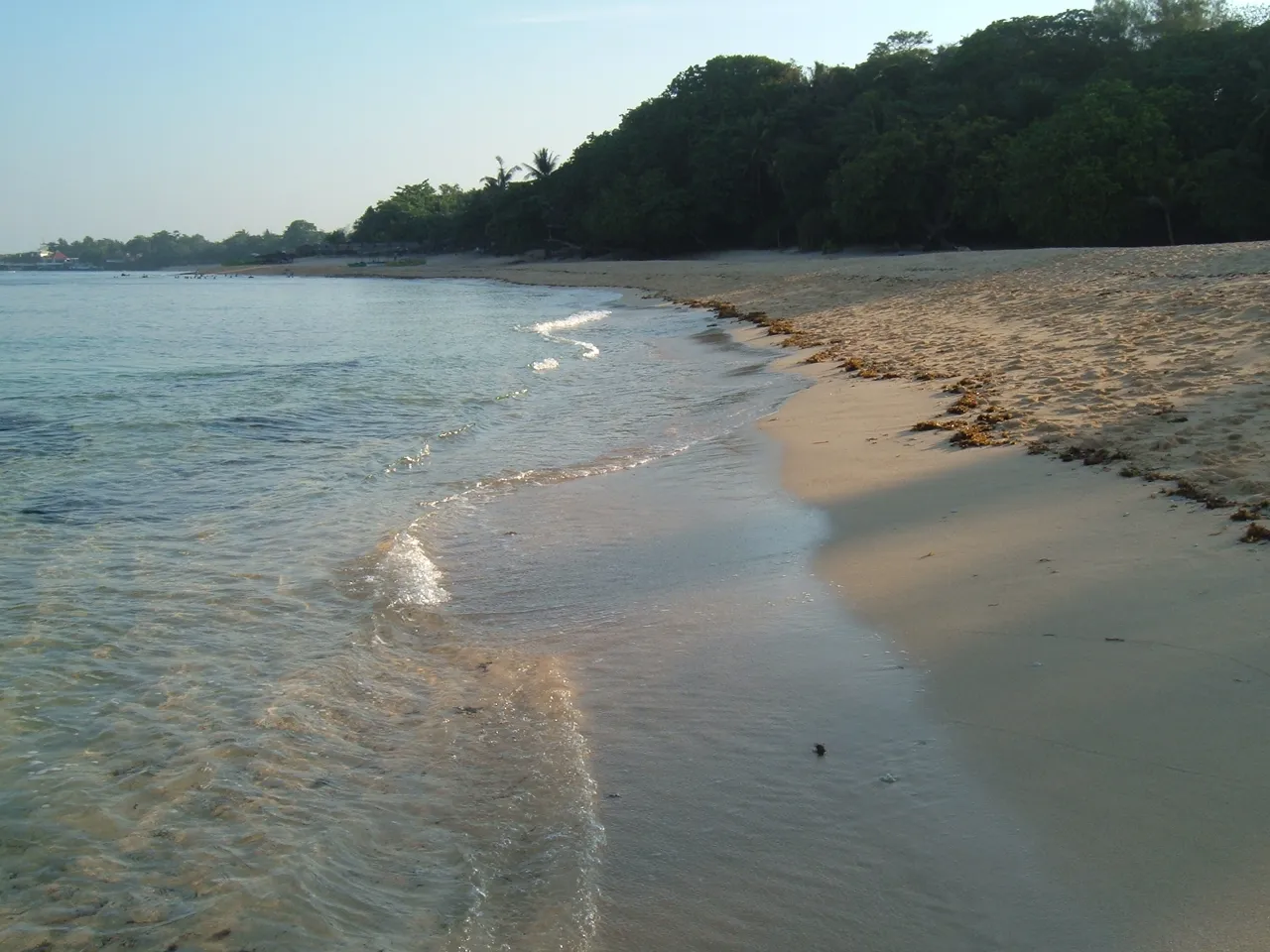 Sandstrand von Patar mit flachen Wellen und bewachsenem Ufer