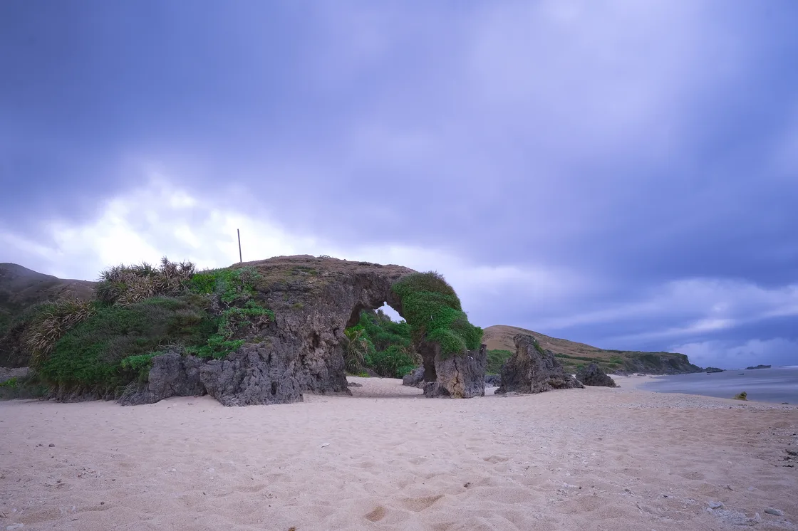 Natürlicher Felsbogen auf hellem Sand am Morong Beach mit Meer und bewachsenem Küstenhang
